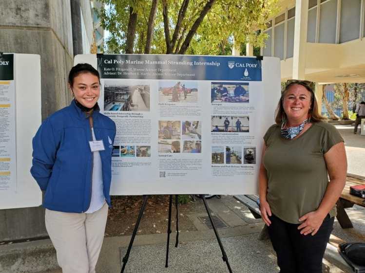 Two people stand in front of a presentation board labeled “Cal Poly Marine Mammal Stranding Internship.”