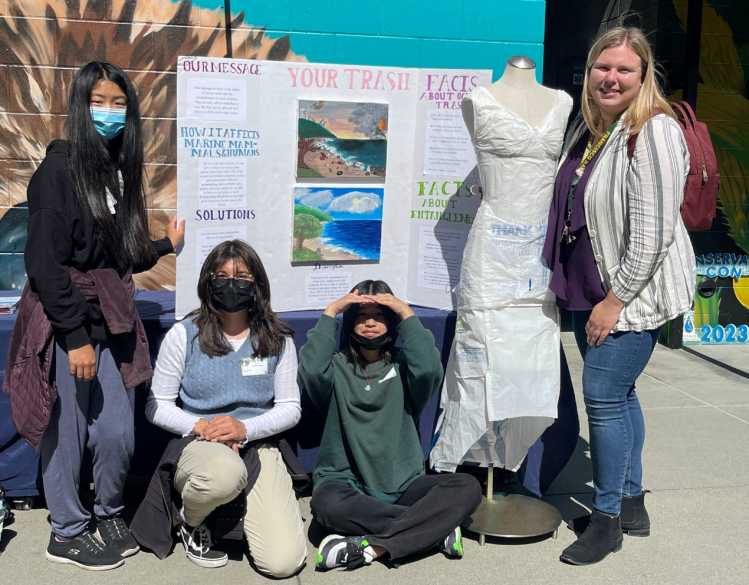 A teacher and three students with their poster.
